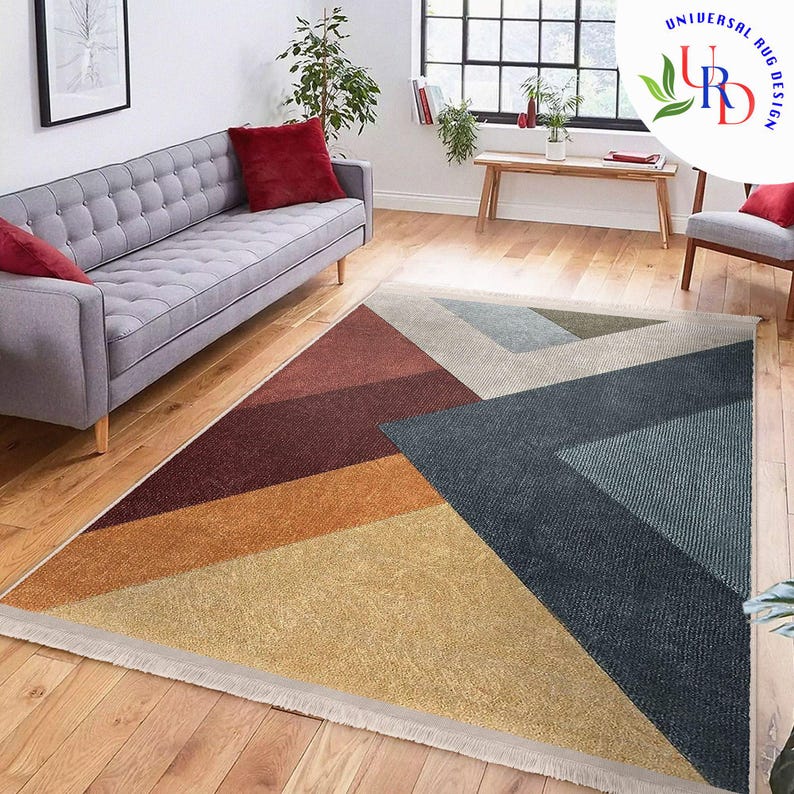 May include: Geometric area rug with a modern design. The rug features a triangular pattern with sections of red, orange, yellow, blue, and gray. The rug is placed on a hardwood floor in a living room setting.