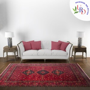 May include: A red, black, and cream patterned rug with a geometric design. The rug is laid out on a wooden floor in front of a white sofa with red pillows.