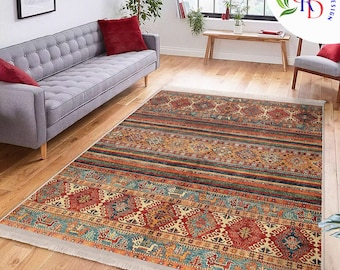 May include: A rectangular area rug with a detailed geometric pattern in shades of red, orange, blue, and beige. The rug features a central design with repeating shapes and borders, and a fringed edge. The rug is placed on a hardwood floor.