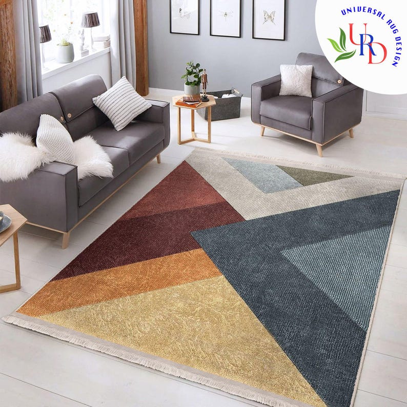 May include: Geometric patterned area rug with a beige fringe. The rug features a design of triangles in shades of red, orange, yellow, blue, and gray. The rug is placed in a living room setting with gray furniture.