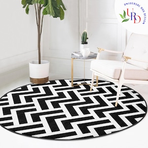 Può includere: Tappeto rotondo geometrico bianco e nero con un motivo ripetitivo di quadrati e rettangoli intrecciati. Il tappeto è su un pavimento bianco con una sedia bianca e un tavolino con una pianta in vaso.