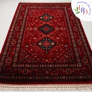 May include: A red rug with a traditional Persian design. The rug has a black and white geometric pattern with a central medallion. The rug has a fringe border.