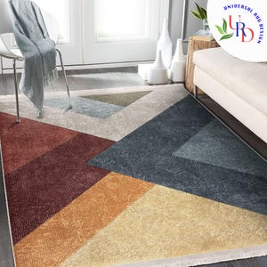 May include: A rectangular area rug with a geometric design. The rug features large triangular and rectangular shapes in shades of red, orange, yellow, blue, and beige. The rug has a fringed edge and is placed on a wooden floor.
