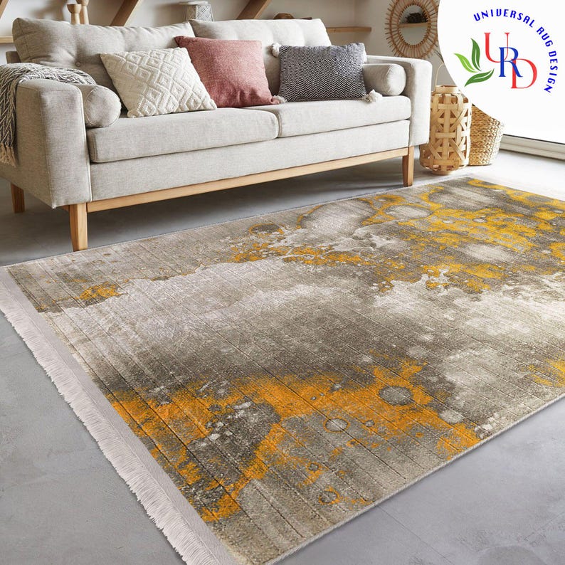 May include: A rectangular area rug with a distressed design. The rug features a gray and yellow color palette with a textured appearance. The rug is placed on a gray floor in front of a beige sofa with decorative pillows.