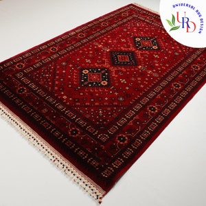May include: A red rug with a traditional Persian design featuring intricate patterns and a central diamond shape. The rug has a white fringe border.