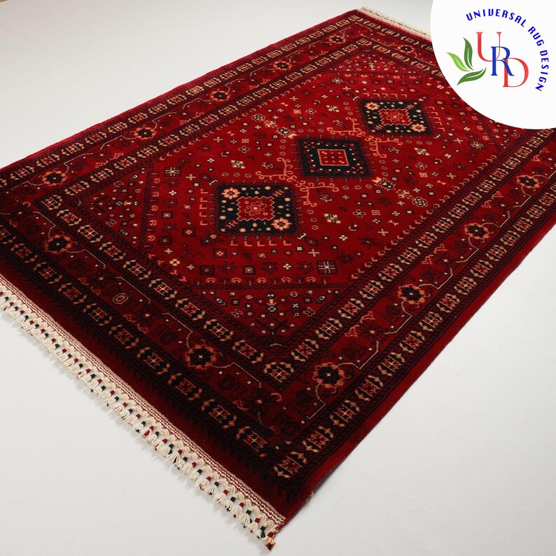May include: A red rug with a traditional Persian design featuring intricate patterns and a central diamond shape. The rug has a white fringe border.