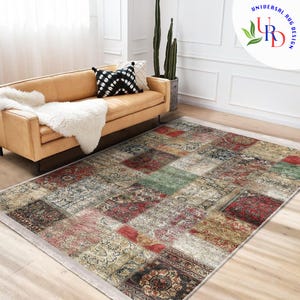 Peut inclure: Un tapis rectangulaire en patchwork avec une variété de motifs et de couleurs, dont le rouge, le vert et le beige. Le tapis est posé sur un sol en bois devant un canapé beige. Le tapis a un aspect vieilli et vintage.