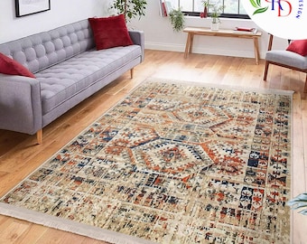 May include: A rectangular area rug with a distressed, vintage-inspired design. The rug features a cream-colored background with a geometric pattern in shades of orange, navy blue, and beige. The rug has a fringed edge and is placed on a hardwood floor.
