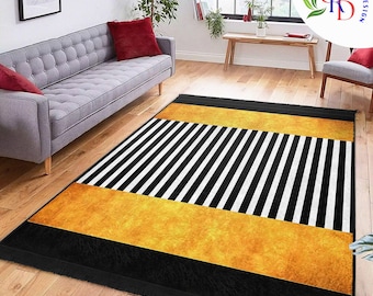 May include: A rectangular rug with a striking design. It has a black border, a central section of black and white stripes, and a gold-coloured textured band. The rug is placed on a wooden floor in a living room.