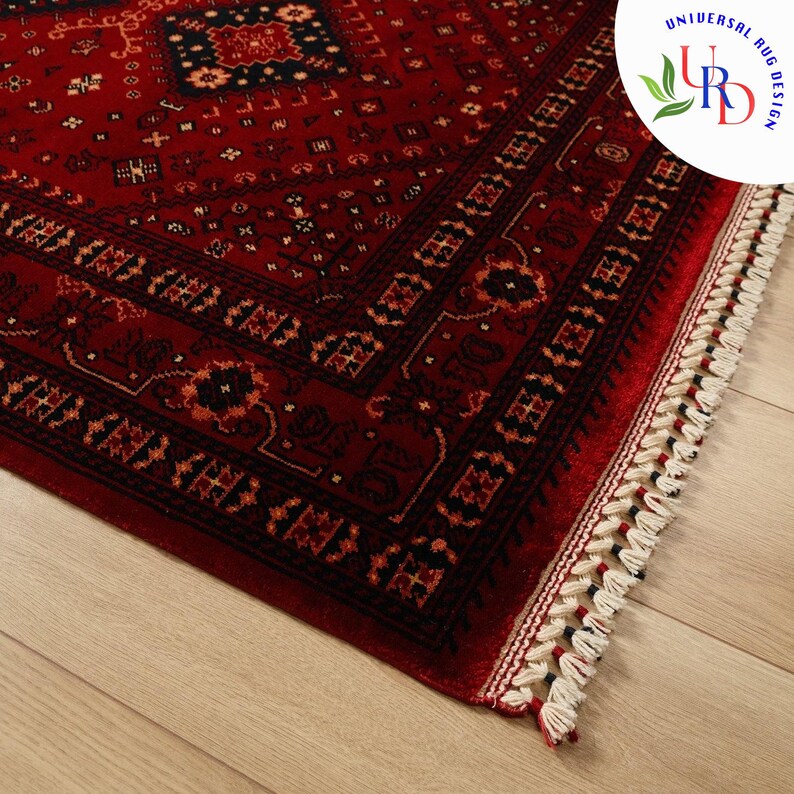 May include: A red rug with a black and gold geometric pattern and a white fringe border. The rug is on a wooden floor.