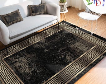 May include: A rectangular black rug with a gold Greek key border. The rug has a distressed, textured appearance with gold and gray accents. The rug is placed in a living room setting with a gray sofa and decorative pillows.
