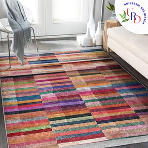 May include: A colorful rectangular rug with a geometric pattern of horizontal and vertical stripes in shades of red, orange, yellow, green, blue, purple, and brown. The rug has a white fringe border.