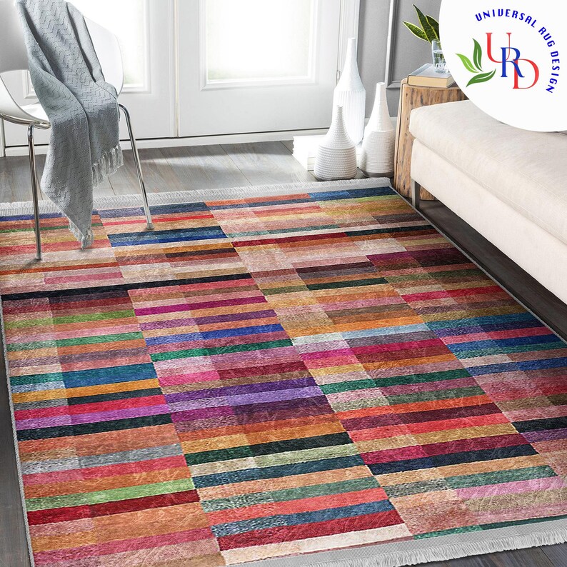 May include: A colorful rectangular rug with a geometric pattern of horizontal and vertical stripes in shades of red, orange, yellow, green, blue, purple, and brown. The rug has a white fringe border.
