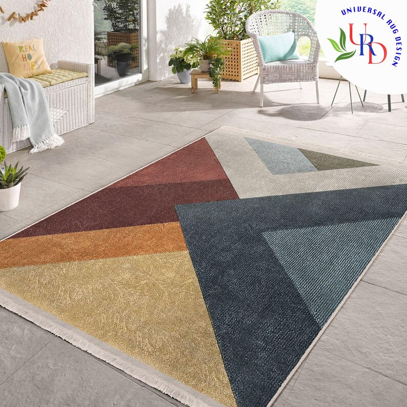 May include: Geometric area rug with a triangular design. The rug features sections of brown, orange, yellow, blue, and gray. The rug has a fringed edge and is placed on a tiled surface. The rug is a modern home decor item.