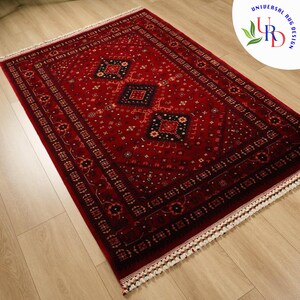 May include: A red rug with a traditional Persian design featuring intricate patterns and a diamond-shaped center. The rug has a white fringe border.