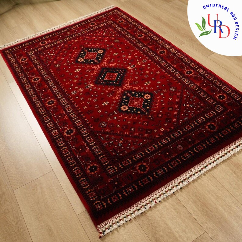 May include: A red rug with a traditional Persian design featuring intricate patterns and a diamond-shaped center. The rug has a white fringe border.
