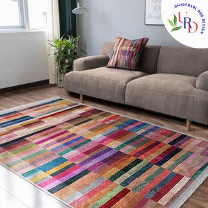 May include: A colorful rectangular rug with a geometric pattern of horizontal stripes in various shades of red, pink, blue, green, and brown. The rug is laid out on a wooden floor in a living room setting with a sofa in the background.