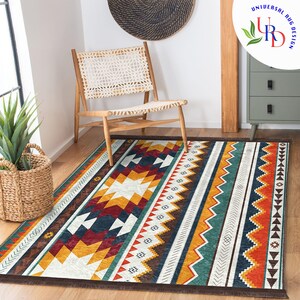 May include: A white and brown area rug with a geometric pattern in shades of red, yellow, blue, and green. The rug has a fringe border and is laid out on a wooden floor with a chair in the background.