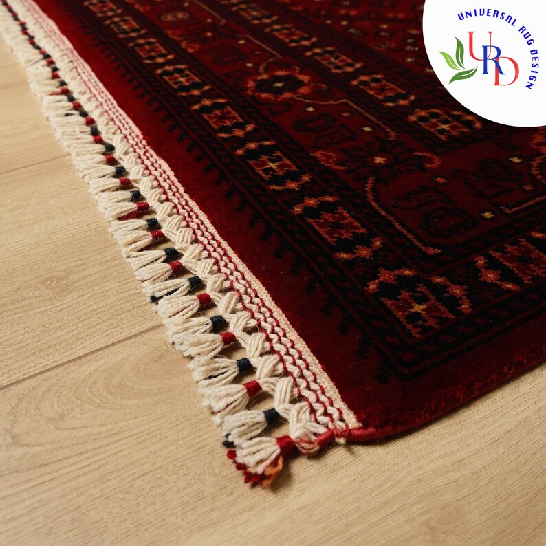 May include: Close-up of a red rug with a traditional Persian design. The rug has a white fringe with black accents.