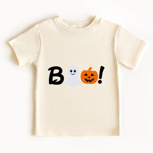 Pode incluir: Uma camiseta de cor creme com um gr&aacute;fico preto de "BOO!" que apresenta um fantasma e uma ab&oacute;bora de Halloween.