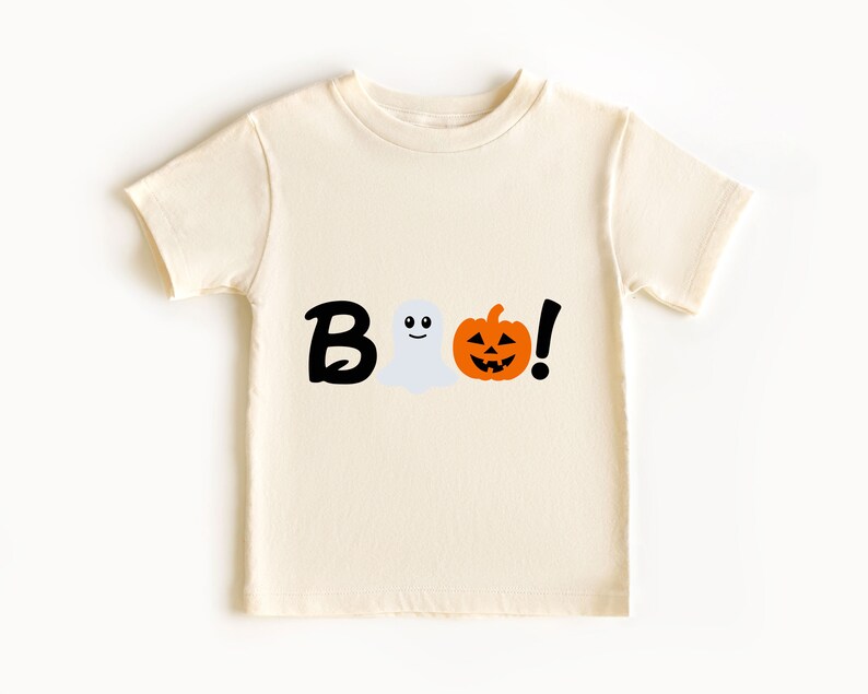 Pode incluir: Uma camiseta de cor creme com um gr&aacute;fico preto de "BOO!" que apresenta um fantasma e uma ab&oacute;bora de Halloween.