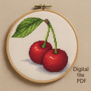 Peut inclure: Broderie au point de croix de deux cerises rouges avec des tiges vertes et une feuille, dans un cercle à broder en bois. Le motif est sur un fond de tissu blanc. Le texte à droite indique "Digital file PDF".