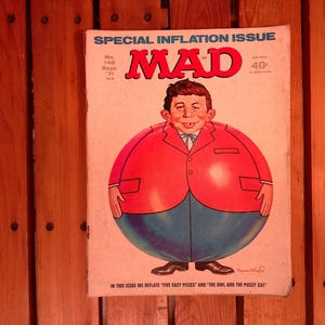 Puede incluir: Portada de la revista MAD vintage con un personaje de dibujos animados con una chaqueta roja y pantalones azules. El título de la revista, "MAD", está en letras rojas grandes. La portada también incluye el texto "SPECIAL INFLATION ISSUE".