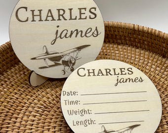 May include: Two wooden baby announcement plaques with a vintage airplane design. The top plaque has the name "CHARLES james" engraved on it. The bottom plaque has the name "CHARLES james" engraved on it and has blank lines for the baby's date, time, weight, and length.