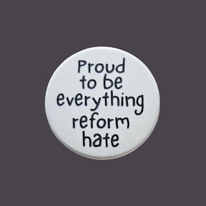 May include: A white circular button with the words "Proud to be everything reform hate" in black. The button is set against a grey background. The text is in a sans-serif font.