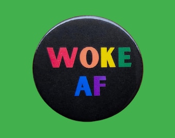 May include: A round, black button with the words "WOKE AF" in rainbow-colored letters. The button is set against a solid green background.