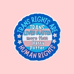 May include: A circular sticker with a scalloped edge featuring a blue border and a central horizontal stripe pattern in light blue, pink, and white. The text reads: TRANS RIGHTS ARE HUMAN RIGHTS and TRANS LIVES MATTER more than Harry Potter.