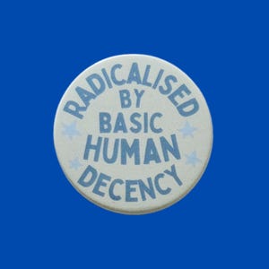 May include: A circular pinback button with a white background and light blue text that reads RADICALISED BY BASIC HUMAN DECENCY. The design includes small light blue stars interspersed between the words, creating a simple and clear graphic.