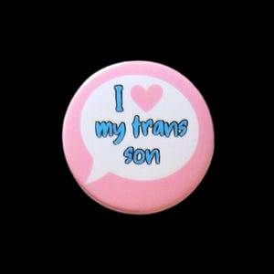May include: Pink button with a white speech bubble that says "I love my trans son" with a pink heart.