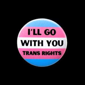 May include: A round button featuring the transgender pride flag colours. The button reads "I'll go with you" in black text and "Trans Rights" in black text.
