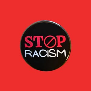 May include: A circular black badge with the words "STOP RACISM" in red and white. The word "STOP" is crossed out with a red line. The background is a solid red colour.
