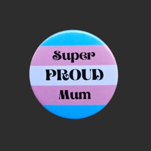 May include: A blue, white and pink button with the text "Super Proud Mum" in black.