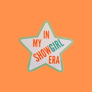 Peut inclure: Autocollant en forme d'étoile blanche avec un bord vert clair. Le texte "IN MY SHOWGIRL ERA" est écrit en orange et turquoise. Le fond est orange.