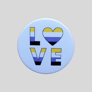 May include: A white button with the word "LOVE" in black and yellow letters. The "O" is replaced with a heart in the colours of the non-binary pride flag: yellow, white, purple, and black.
