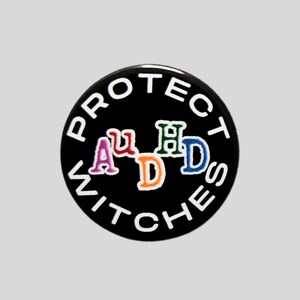 May include: A circular black pin featuring the white text PROTECT WITCHES curved around the border. In the centre, the letters AuDHD are displayed in a stylised font with each letter in a different colour: pink, red, green, orange, and blue.