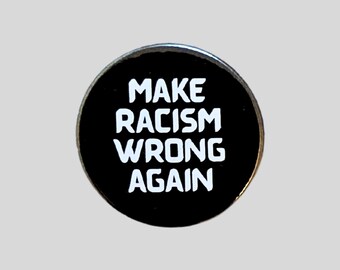 May include: A round, black pin with the white text "MAKE RACISM WRONG AGAIN". The pin has a shiny, metallic border and is set against a light gray background. The text is in a bold, sans-serif font.