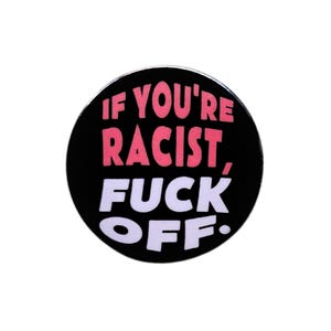 May include: A circular pin-back button with a black background. The text "IF YOU'RE RACIST," is printed in bold pink capital letters on the top half, and the text "FUCK OFF." is printed in bold white capital letters on the bottom half.