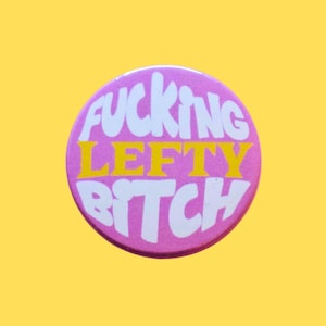 May include: A circular, pink badge with the text "FUCKING LEFTY BITCH" in white and yellow. The badge is set against a yellow background.