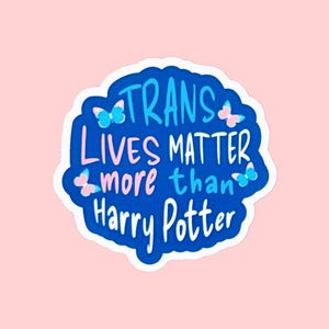 May include: A die-cut sticker with a dark blue background featuring the white and pink text TRANS LIVES MATTER more than Harry Potter. The design includes small light blue and pink butterfly illustrations scattered around the lettering.