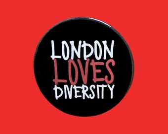 May include: A round black button with the words "LONDON LOVES DIVERSITY" in white and red lettering. The button is set against a solid red background.