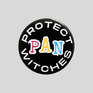 May include: A circular black pinback button featuring the white text "PROTECT" arched across the top and "WITCHES" arched across the bottom. In the centre, the word "PAN" is displayed in large, colourful letters with pink, yellow, and blue.