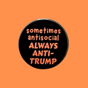May include: A black button with the words "sometimes antisocial ALWAYS ANTI-TRUMP" in orange lettering. The button is set against an orange background.