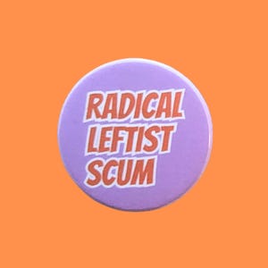 May include: A circular, lilac button featuring the text "RADICAL LEFTIST SCUM" in orange with a white outline. The button is displayed on an orange backdrop.