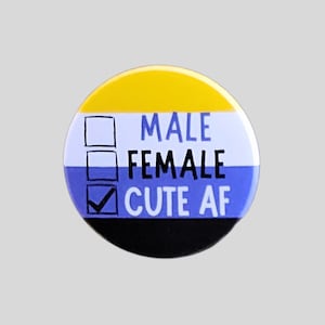 May include: A circular pinback button featuring horizontal stripes of yellow, white, blue, and black. The text reads MALE, FEMALE, and CUTE AF next to three square checkboxes. The third checkbox contains a black checkmark symbol.