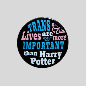 May include: A circular black pin badge displaying the text "TRANS Lives are more IMPORTANT than Harry Potter" in blue, pink, and white typography, decorated with a small pink butterfly illustration and a tiny blue butterfly icon.