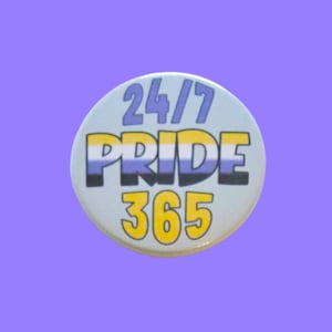 May include: A round button with the text "24/7 PRIDE 365" in blue, yellow, and black. The button has a light blue background and is set against a purple background. The text is in a bold, sans-serif font.